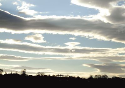 Dramatic sky with layered clouds over a landscape of trees; Gallery Two