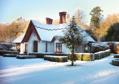 Snow-covered cottage with red trim and chimneys; winter scene