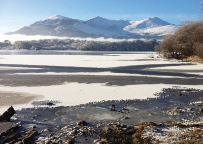 Snow-covered mountains reflected in a partially frozen lake on a clear day