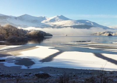 Snow-covered mountains and partially frozen lake in a winter landscape.