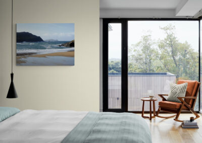 Coastal bedroom with beach scene art, rocking chair, and large windows.