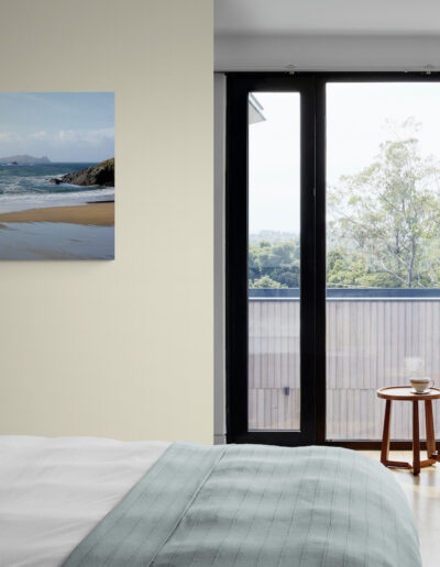 Coastal bedroom with beach scene art, rocking chair, and large windows.