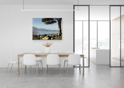 Modern dining room with minimalist furniture, framed landscape, and modern kitchen design.