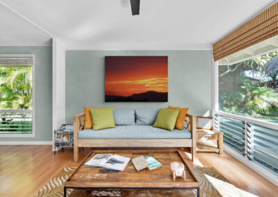 Living room with tropical decor, featuring a wooden sofa, sunset artwork, and natural light.