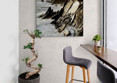 Modern interior with coastal decor: art print of rocky coastline, bonsai tree, and bar seating.