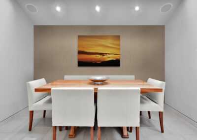 Modern dining room with wooden dining table, white chairs, and sunset art. Pauline Christie.
