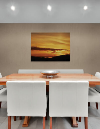 Modern dining room with wooden dining table, white chairs, and sunset art. Pauline Christie.