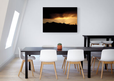 Modern dining room with black table and white chairs, featuring landscape art.