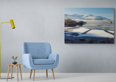 Modern living room with blue armchair, floor lamp, side table, and winter landscape art.