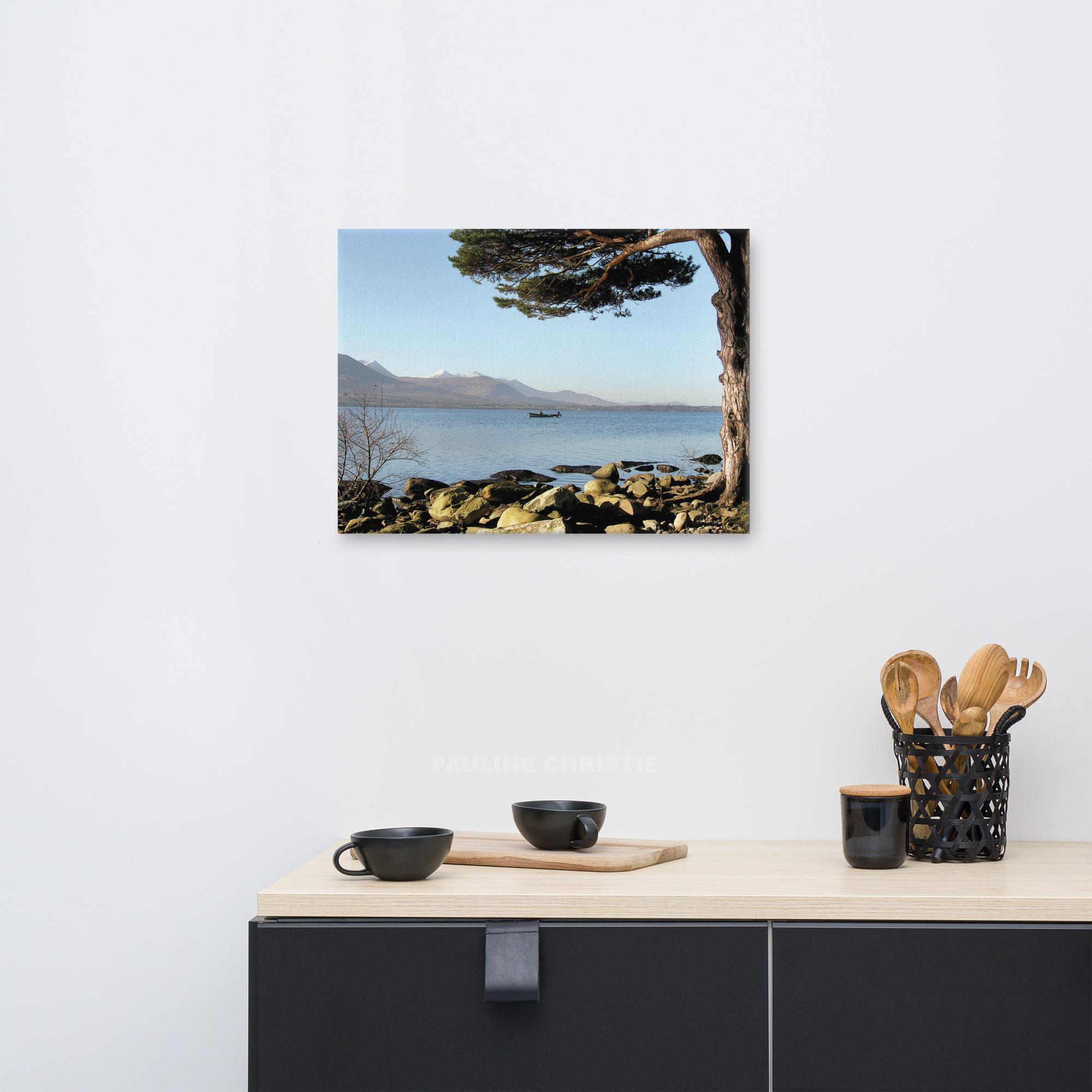 Lone boat on Killarney Lakes, with mountains and a tree in the background.